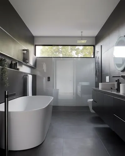 Dark bathroom with a freestanding white bathtub, black vanity and frosted glass partition