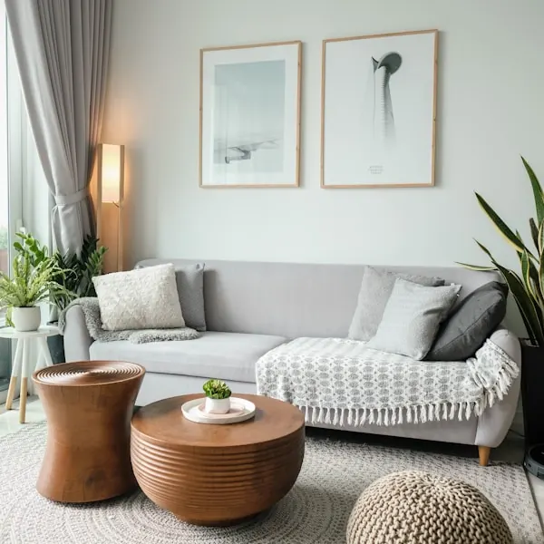 Living room with a grey sofa, timber drum stools, a woven pouf and framed art