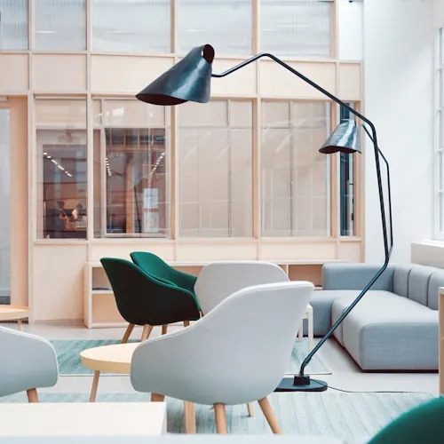 Office breakout area with teal and white lounge chairs, an arched floor lamp and glazed partitions