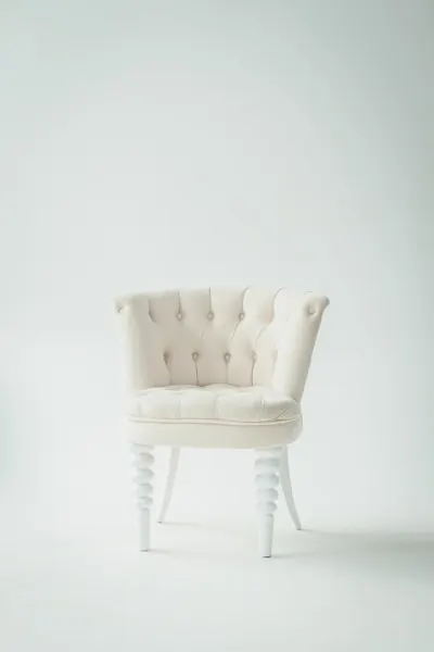 White button-tufted armchair with turned legs against a pale wall
