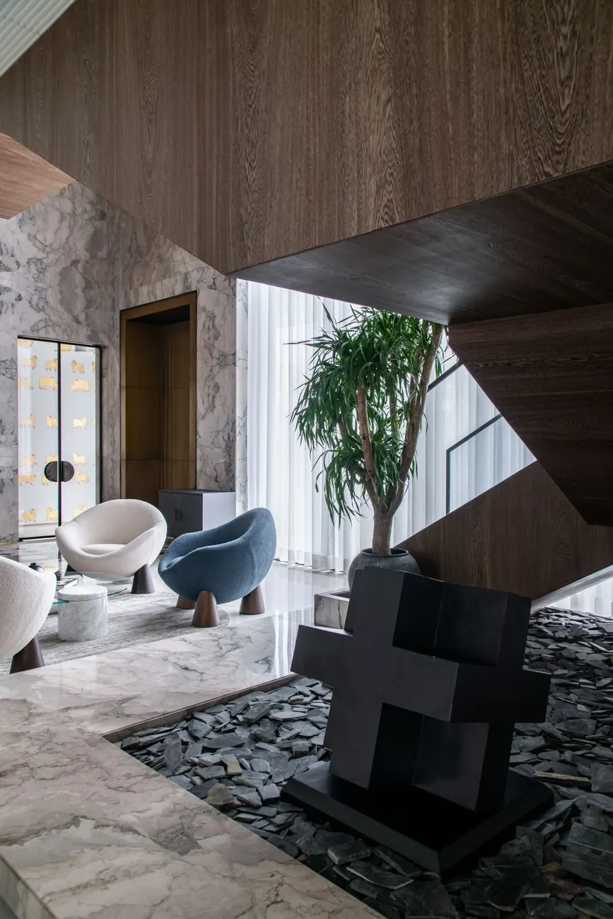 Double-height lounge with sculptural chairs, a dark timber stair and tall glazing