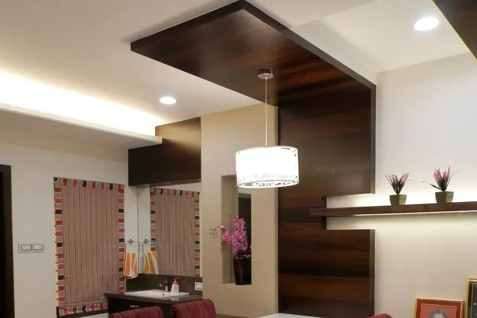 Dining area with a dark timber dropped ceiling panel, recessed downlights, a white drum pendant over the table and maroon upholstered chairs