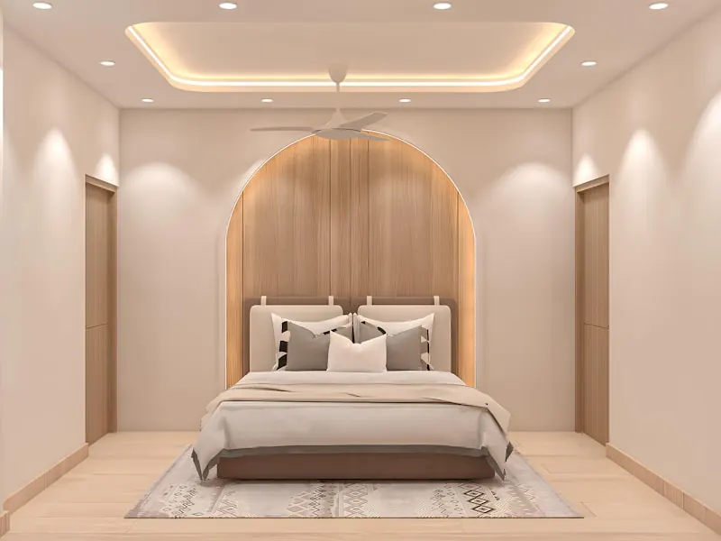 Bedroom with a recessed tray false ceiling lit by a warm cove light, wall-washer spotlights and an arched timber-panelled headboard wall behind the bed