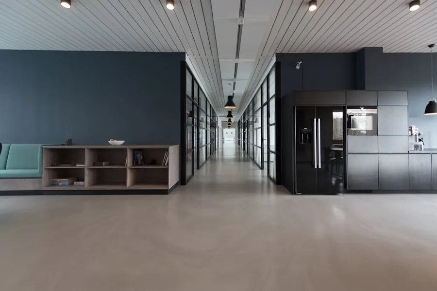 Long open interior with large-format light grey floor tiles, a slatted ceiling with recessed lights, glass partitions and dark built-in cabinetry