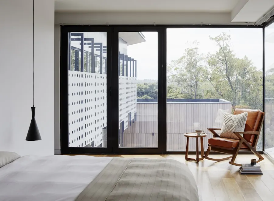 Bedroom corner with full-height black-framed glass doors opening to a balcony, a wooden rocking chair with an orange cushion and a black pendant lamp