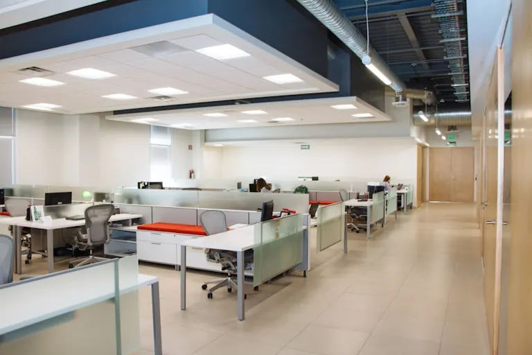 Open-plan office floor with exposed ceiling services, white workstations and red accent screens