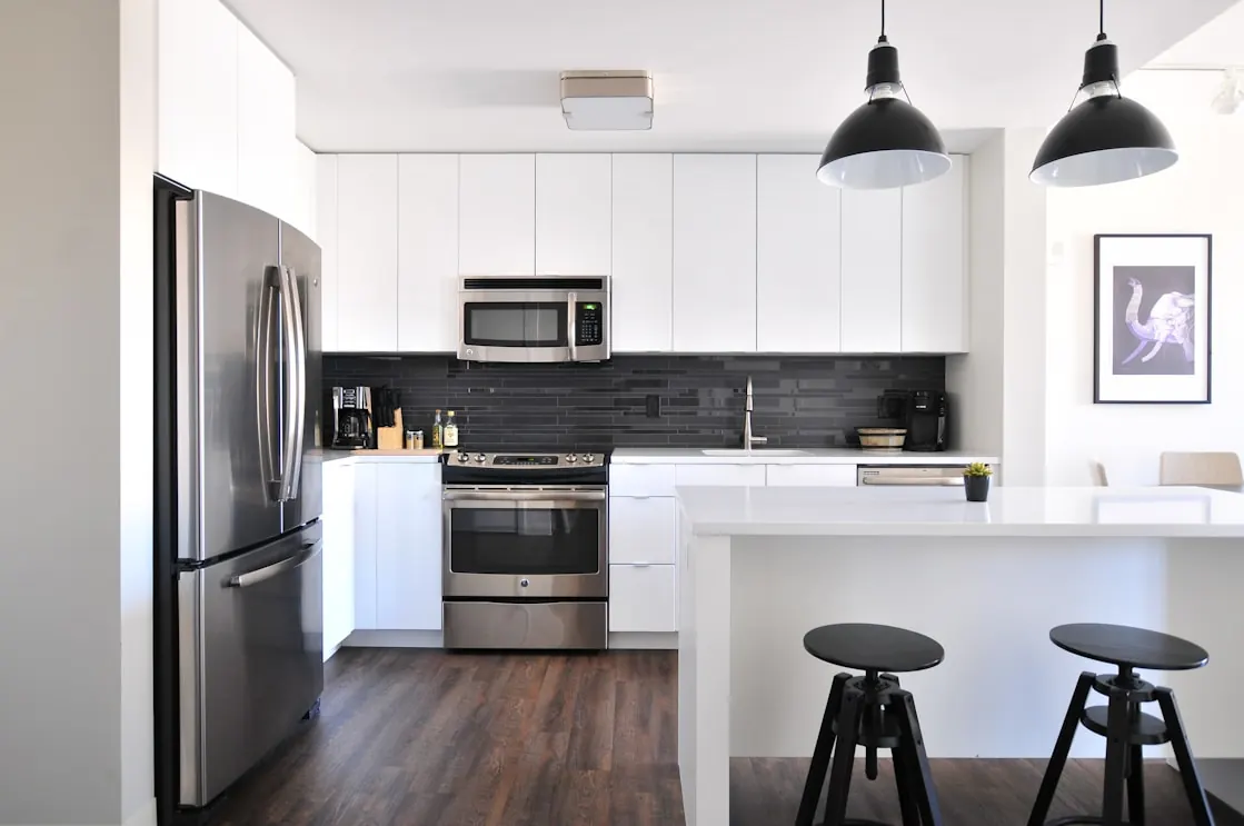 White modular kitchen with dark tile splashback, island counter and black pendant lights