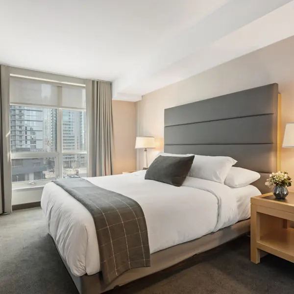 Bed with a tall grey padded headboard, white linen and a timber bedside table