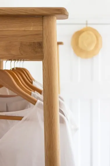 Light wooden clothes rail with wooden hangers and a straw hat