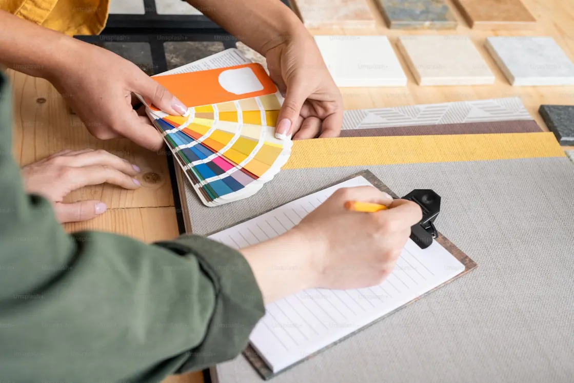 Designer comparing a colour fan with laminate and stone samples while noting selections